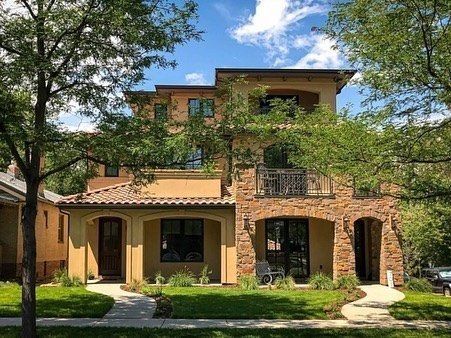Three-story home with stucco exterior, stone accents, and a balcony, viewed from the front yard.