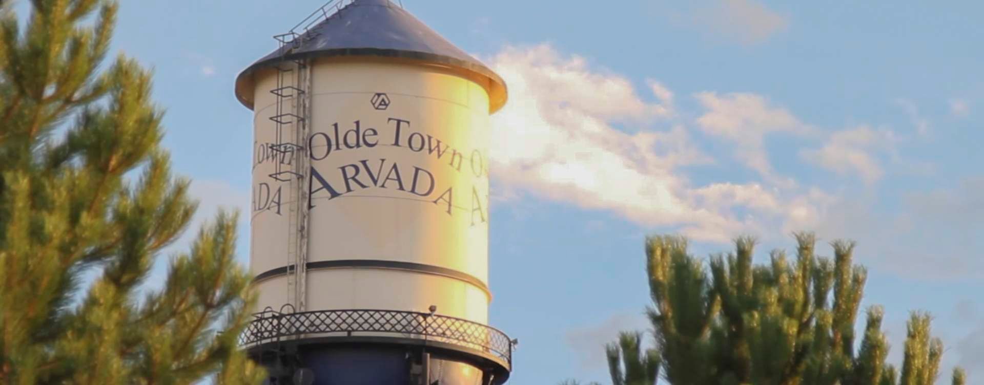 Water tower in Olde Town Arvada against a blue sky with clouds.
