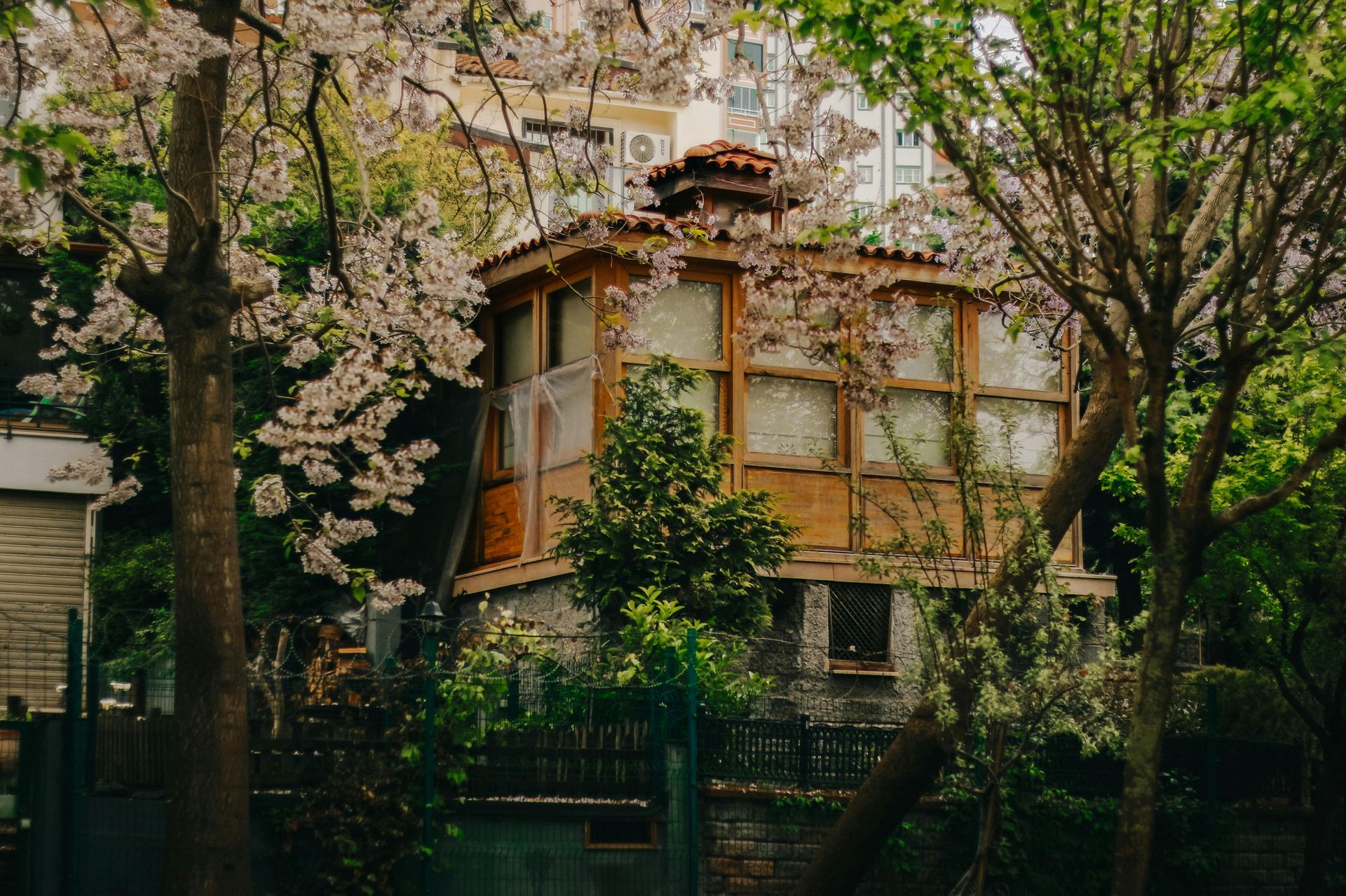 A small stone house surrounded by blooming trees and greenery in a quiet garden setting.