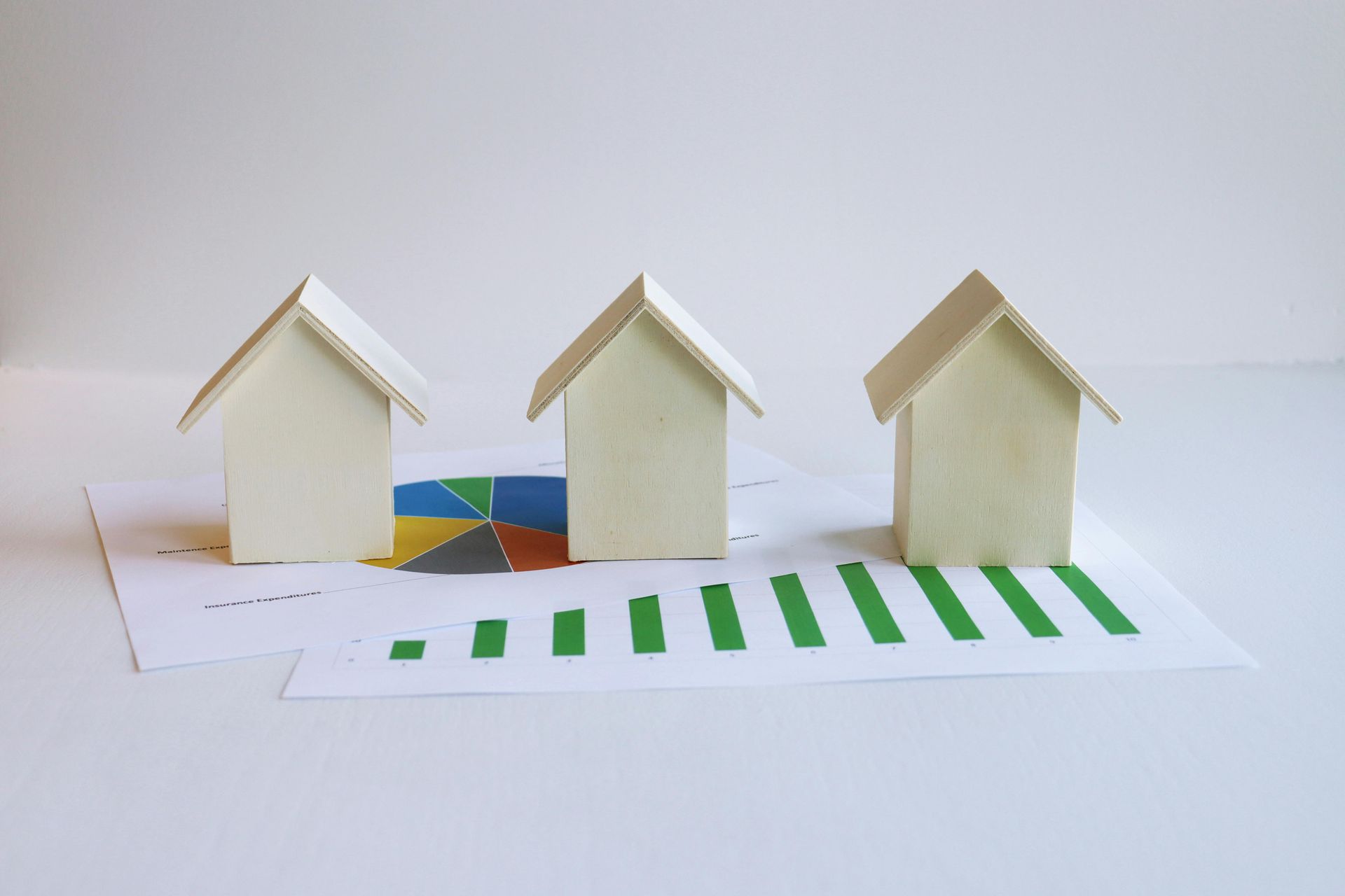 Three small white paper house models on a white surface with green striped paper in front
