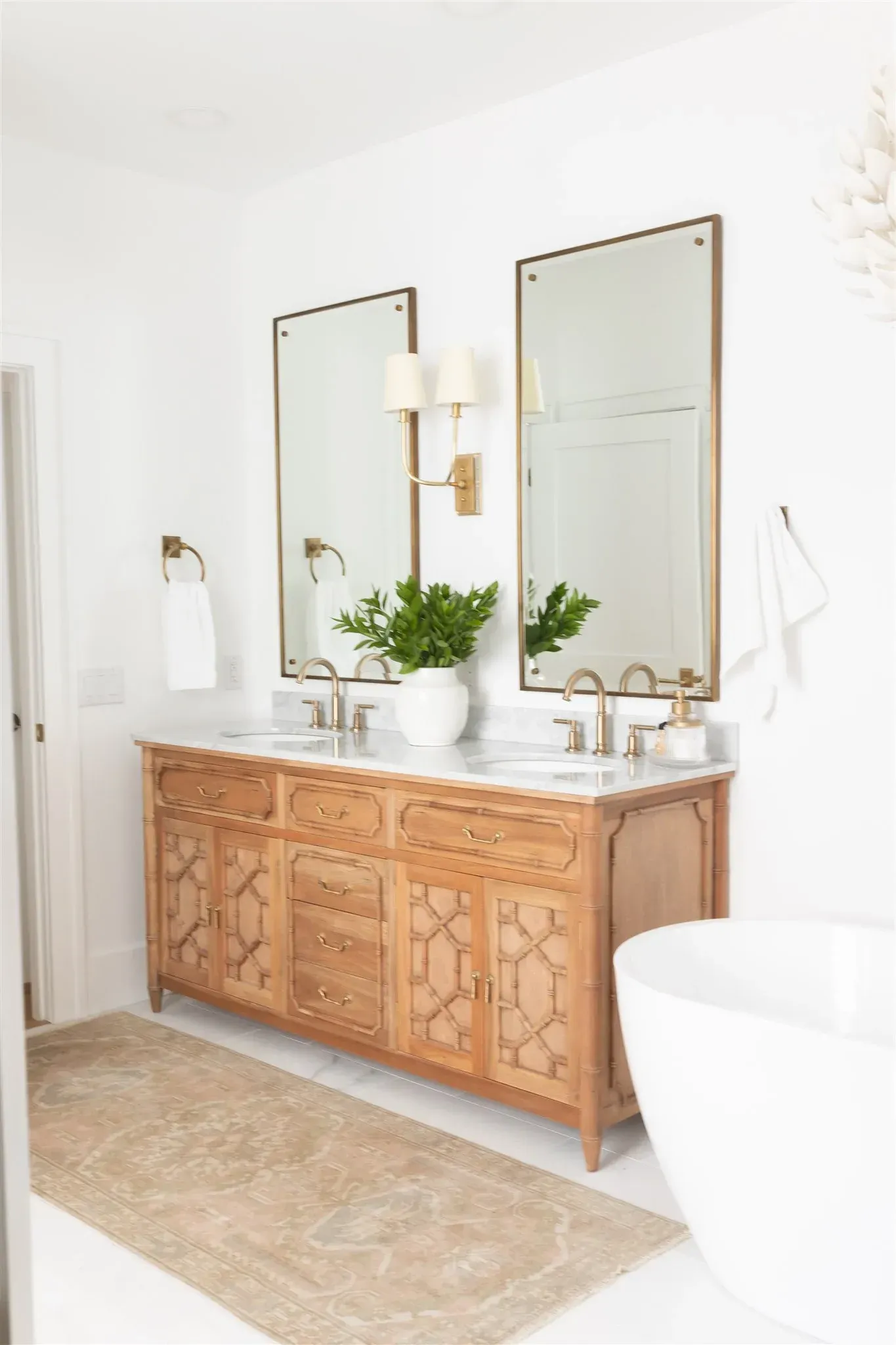 Bathroom with light wood vanity, marble countertop, rectangular mirrors, sconces, and rug.