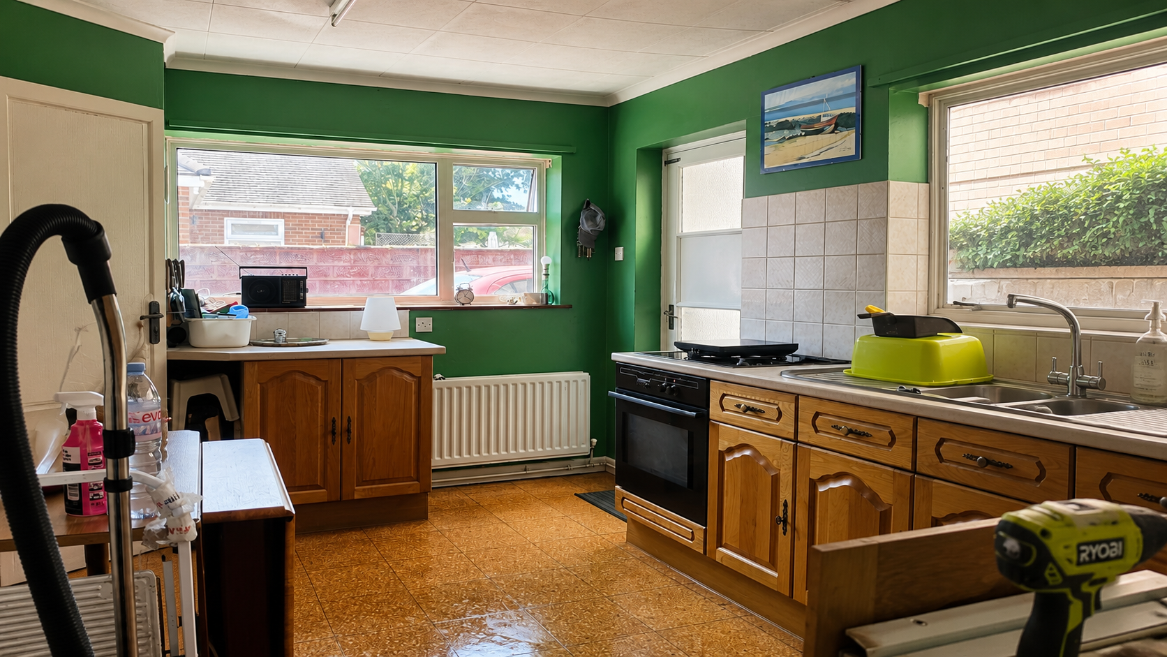 Bright green kitchen with wooden cabinets, stove, sink, and large windows letting in daylight