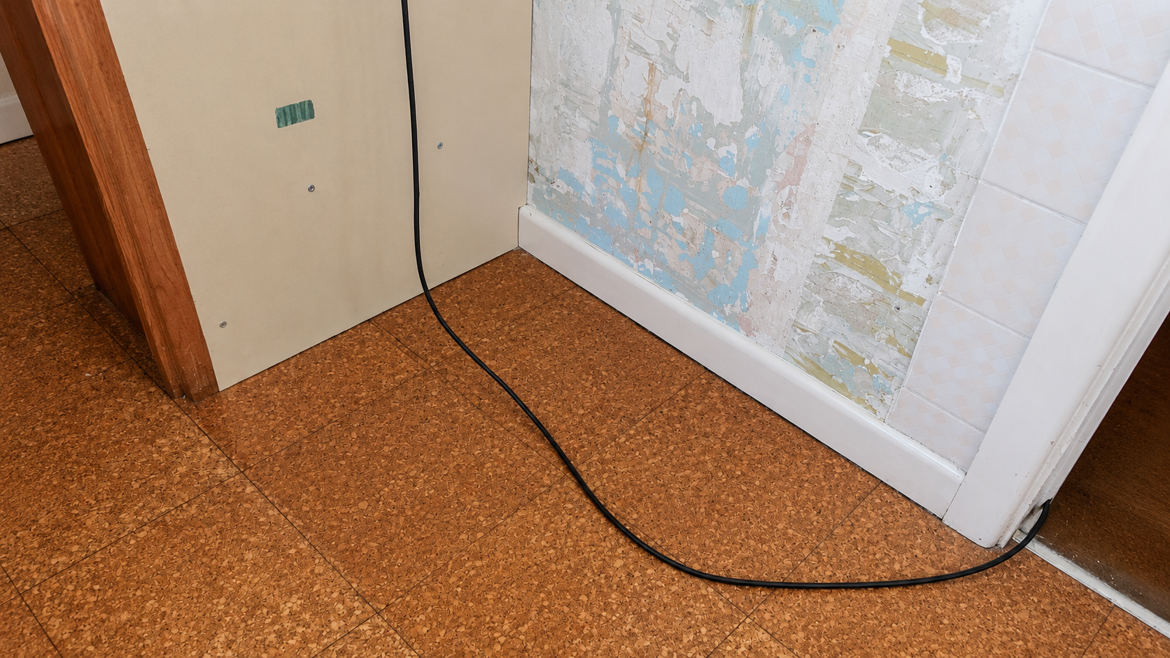 Hallway corner with a beige cabinet, black cable on a speckled floor, and a door with maps/posters.