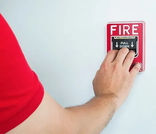 A person is pressing a fire alarm button on a wall.