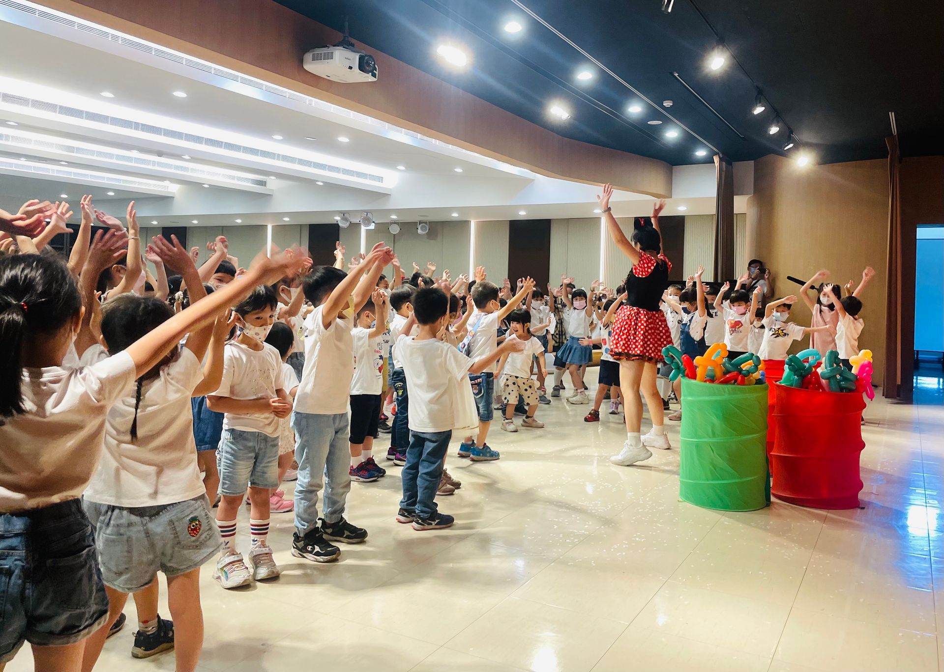 A group of children are dancing in a large room.