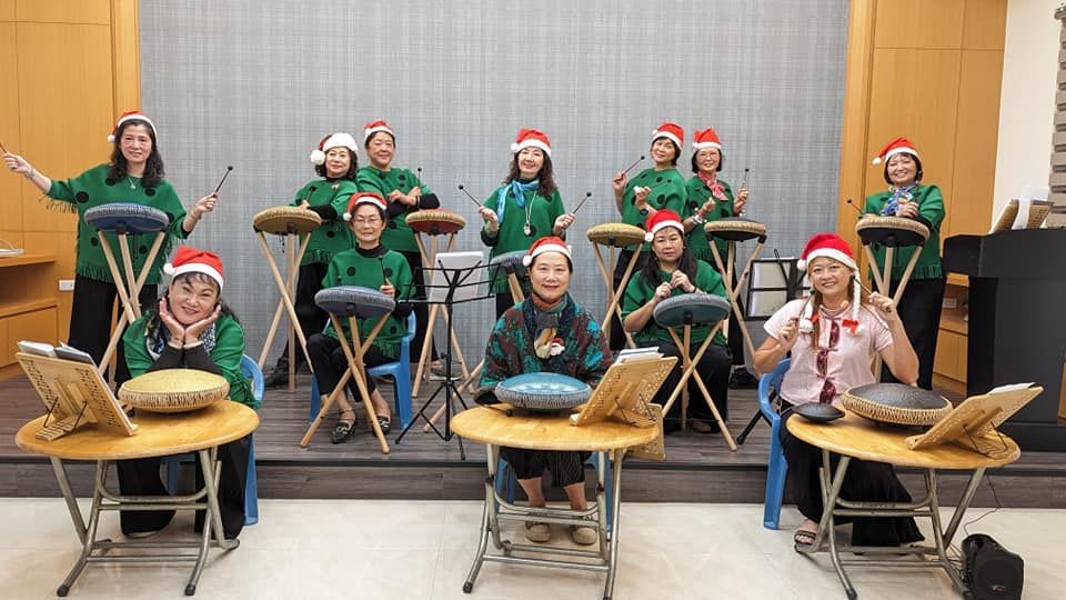 A group of women wearing santa hats are sitting at tables playing instruments.