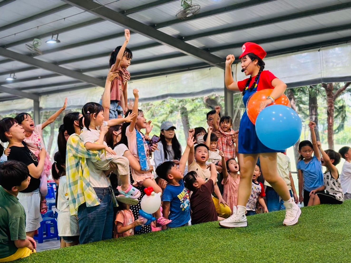 A clown is holding a blue balloon in front of a crowd of children.