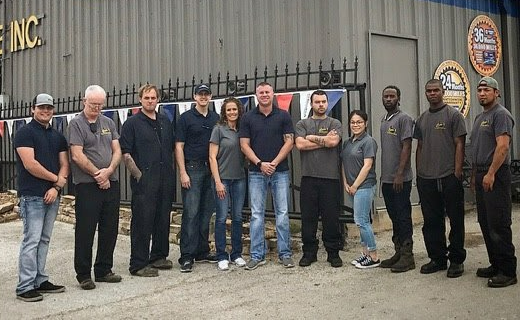 Group of people standing outside a building. Several are wearing matching shirts, some are smiling.