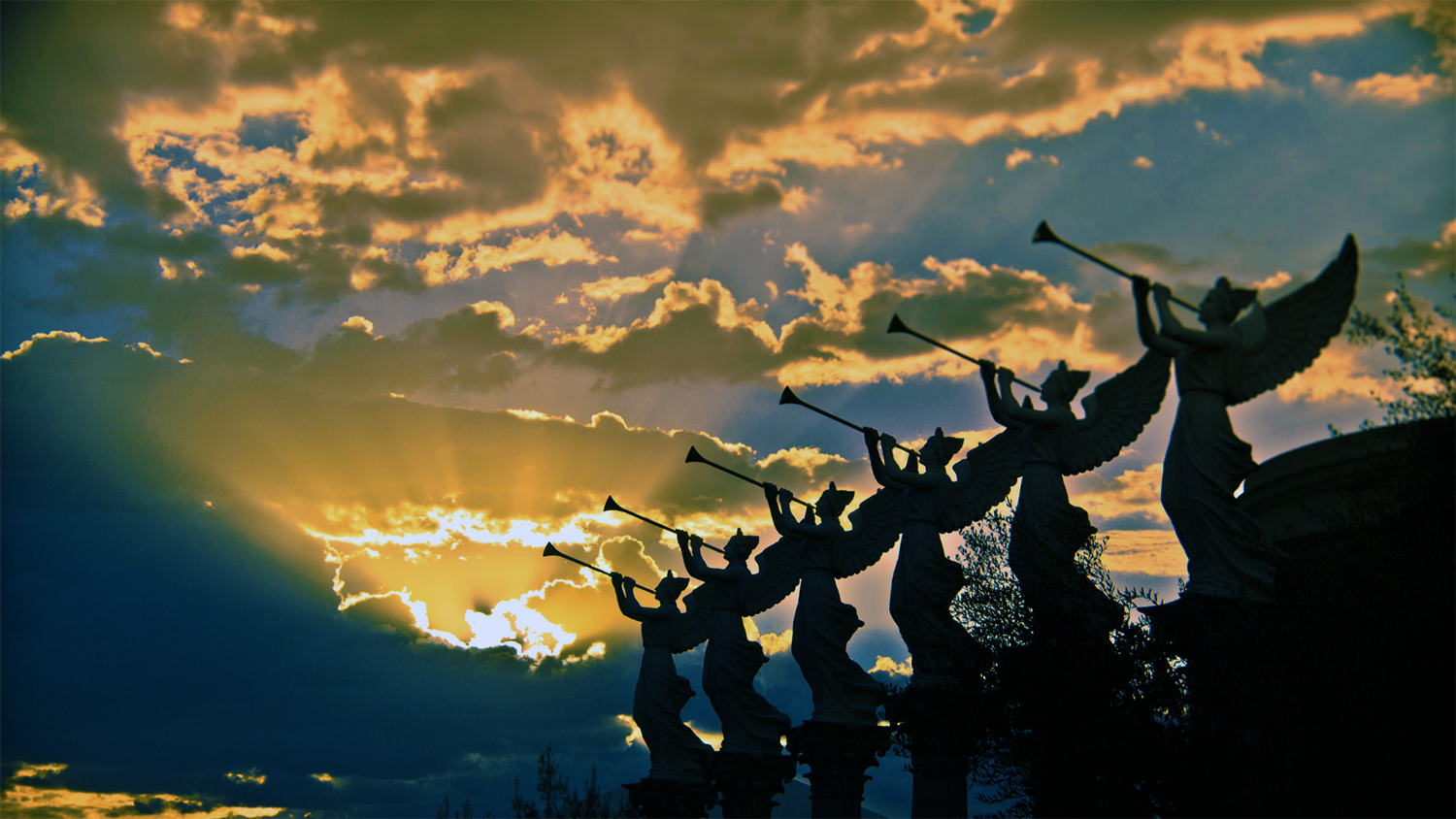 Silhouetted dancers with raised arms against a dramatic orange sunset sky