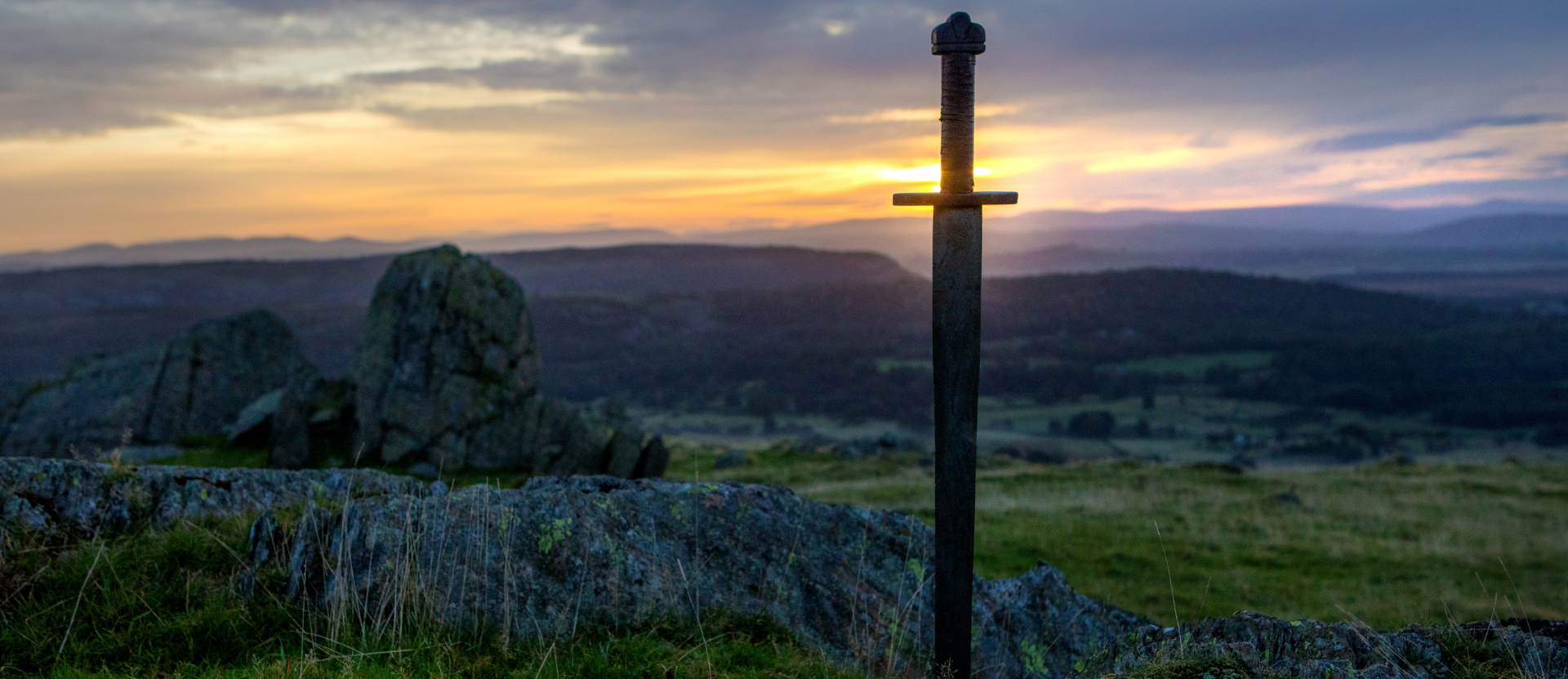 Sunset over a rocky hillside with a stone cross silhouetted in the foreground