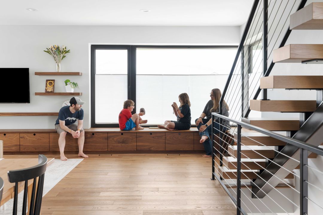A family is sitting on a window sill in a living room next to stairs.