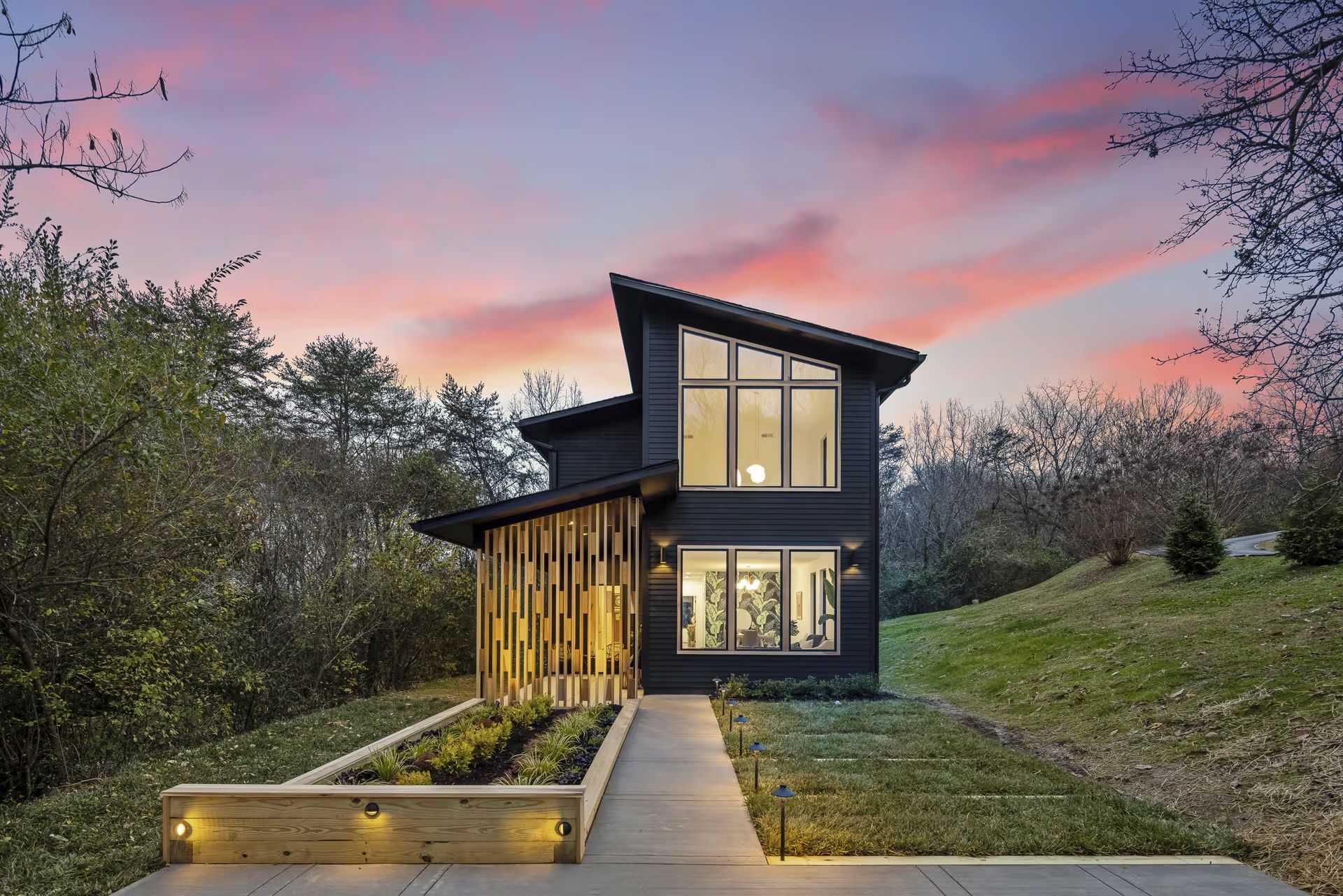 A black house is sitting on top of a hill with a sunset in the background.