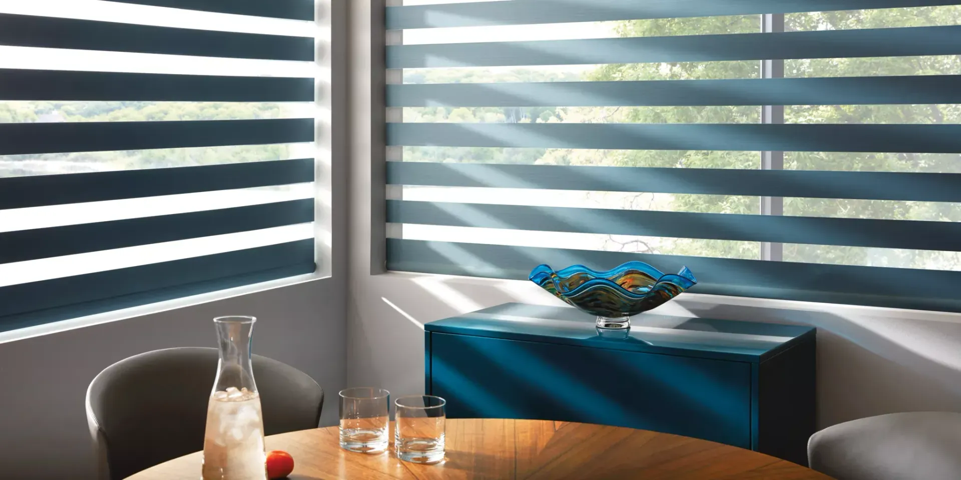 A dining room with a table and chairs and a window with striped blinds.