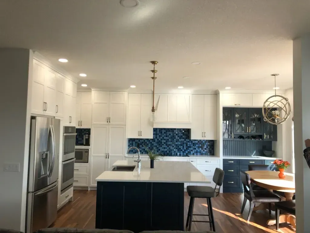 A kitchen with white cabinets , stainless steel appliances , a large island and a dining table.