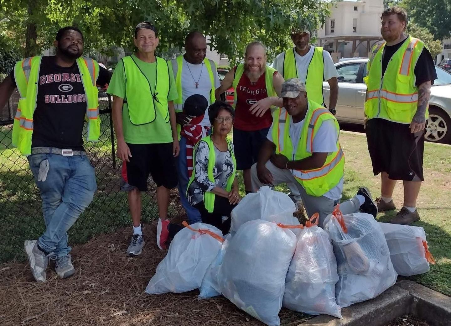 Volunteers in neon safety vests posing with trash bags during a roadside cleanup