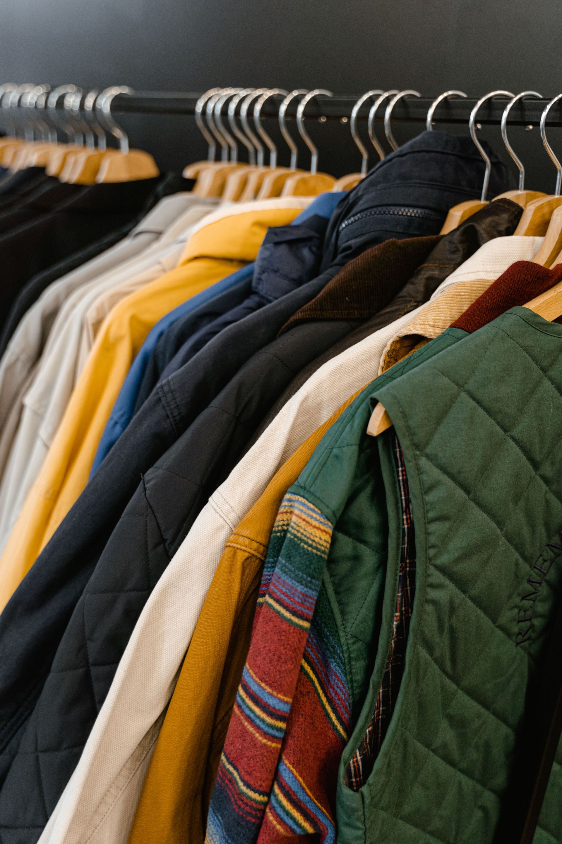 Clothes hanging on a rack, including jackets and coats in green, yellow, black, and denim.