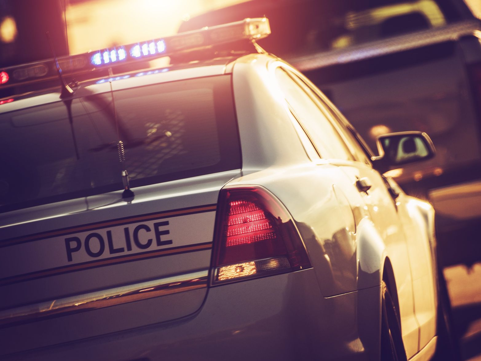 Police car with flashing lights, sunlight, rear view.