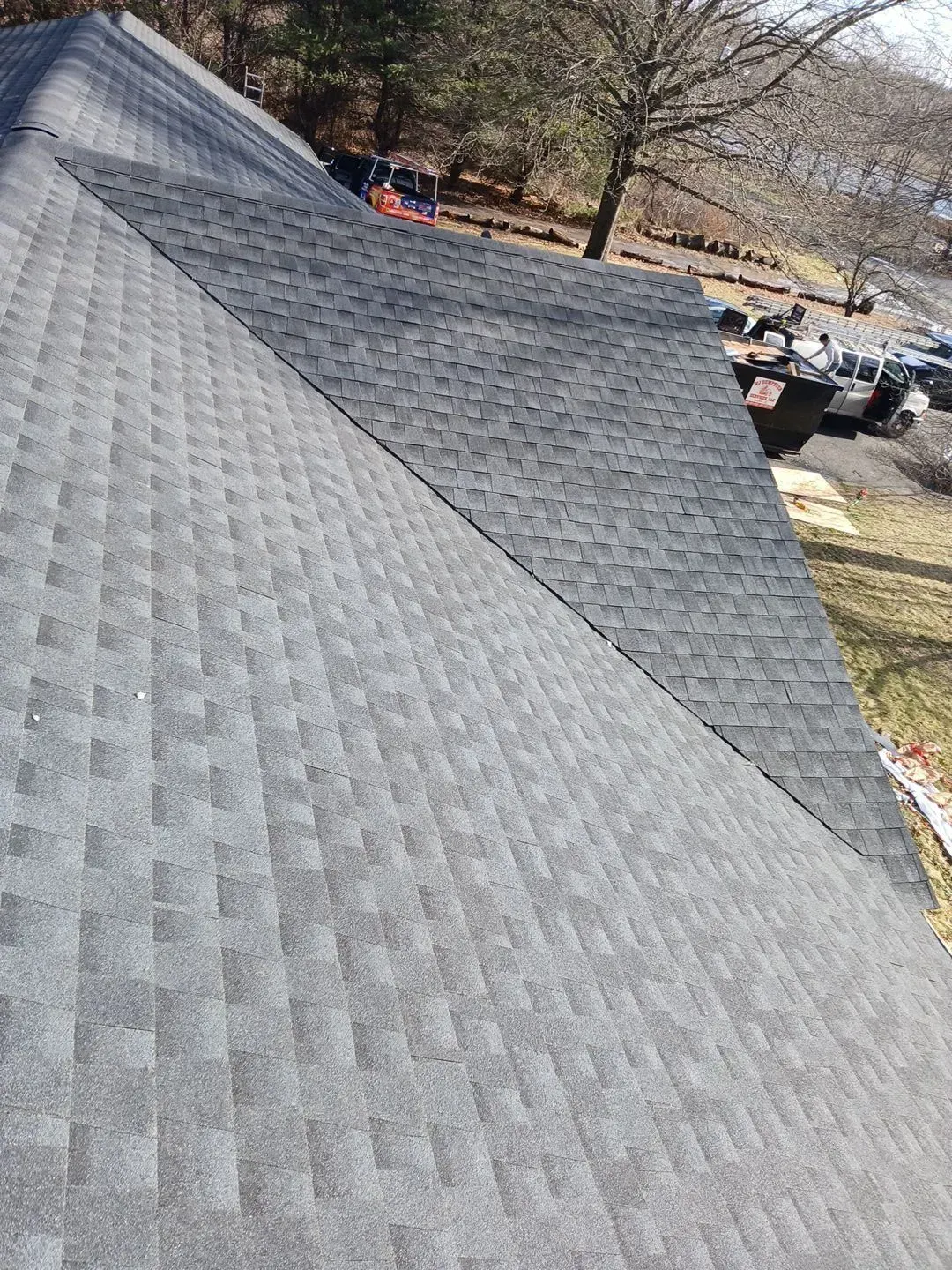 Gray asphalt shingle roof on a house, angled view. One side appears newer than the other.