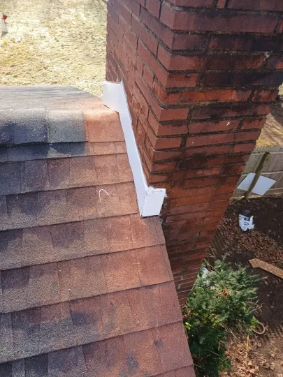 Brick chimney with white flashing on a brown shingle roof.
