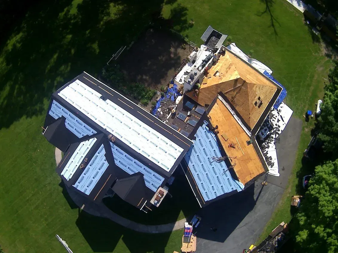 Aerial view of a house undergoing roof replacement; various sections with new shingles, others with exposed underlayment.