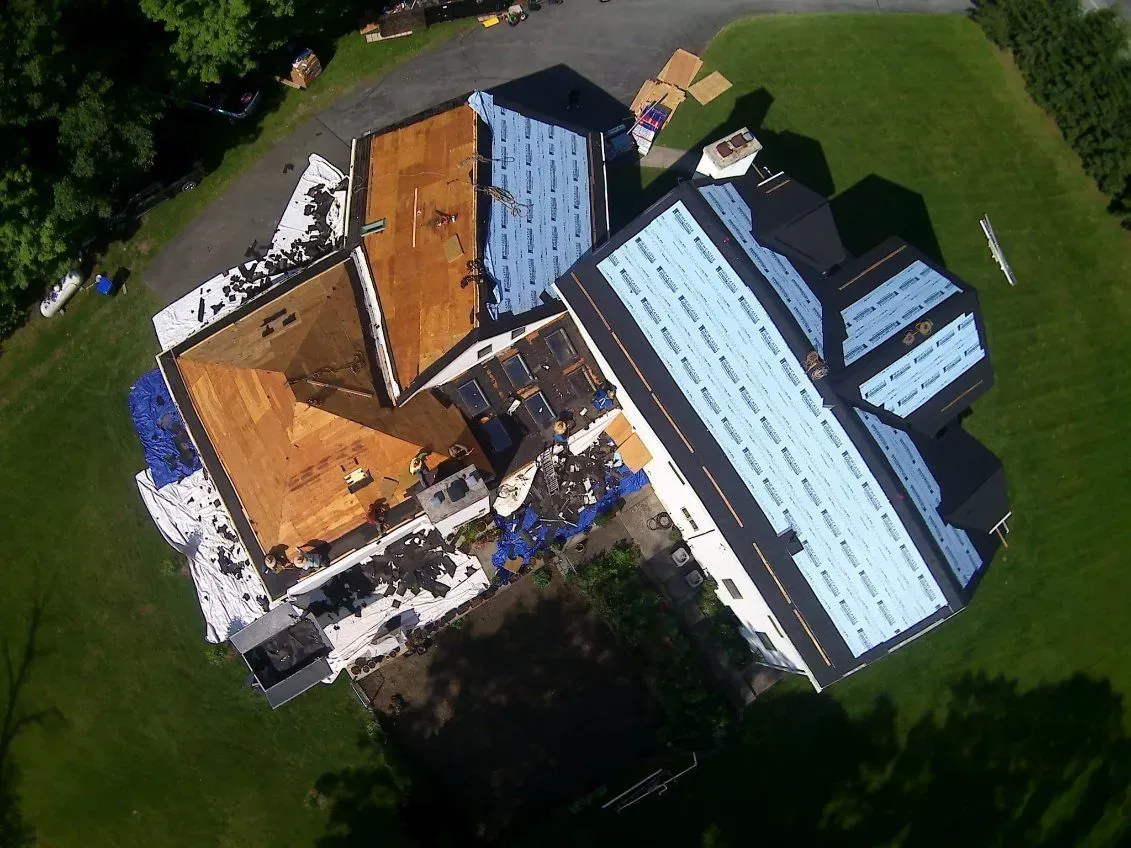 Aerial view of a house undergoing roof replacement, with sections of old and new roofing visible.