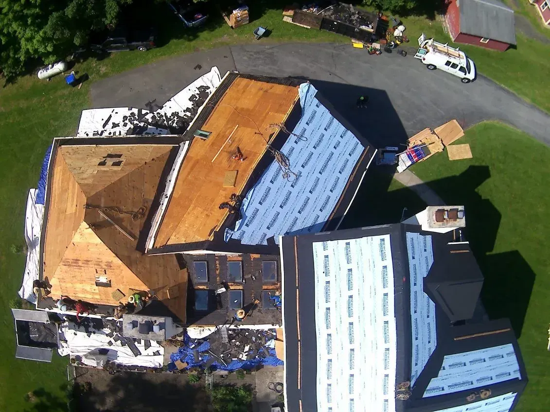 Roof of a house under construction; part covered with brown shingles, part with blue underlayment.