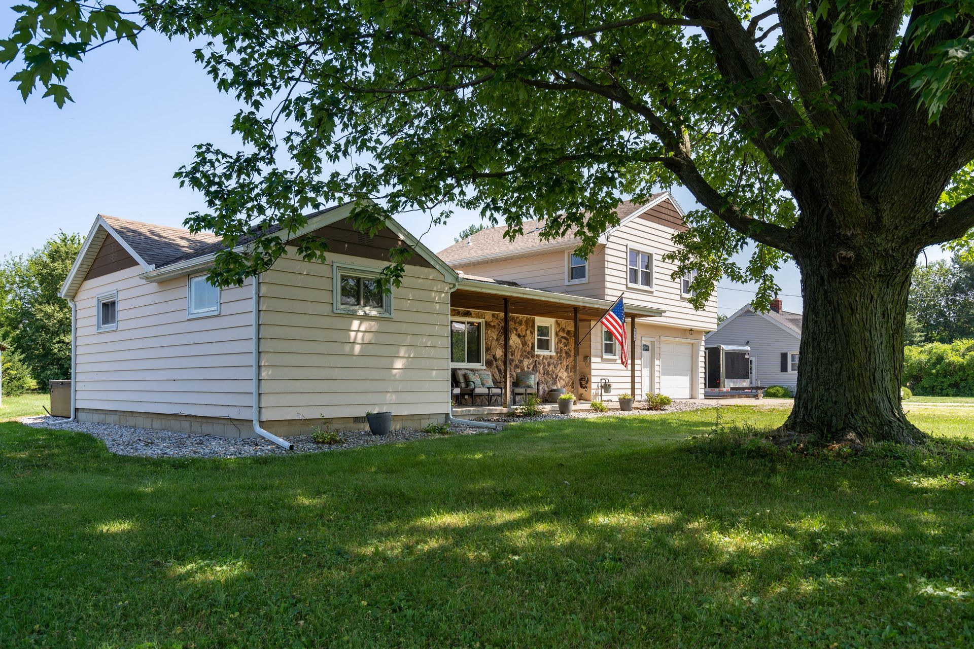 White house with porch and large tree in a sunny green yard
