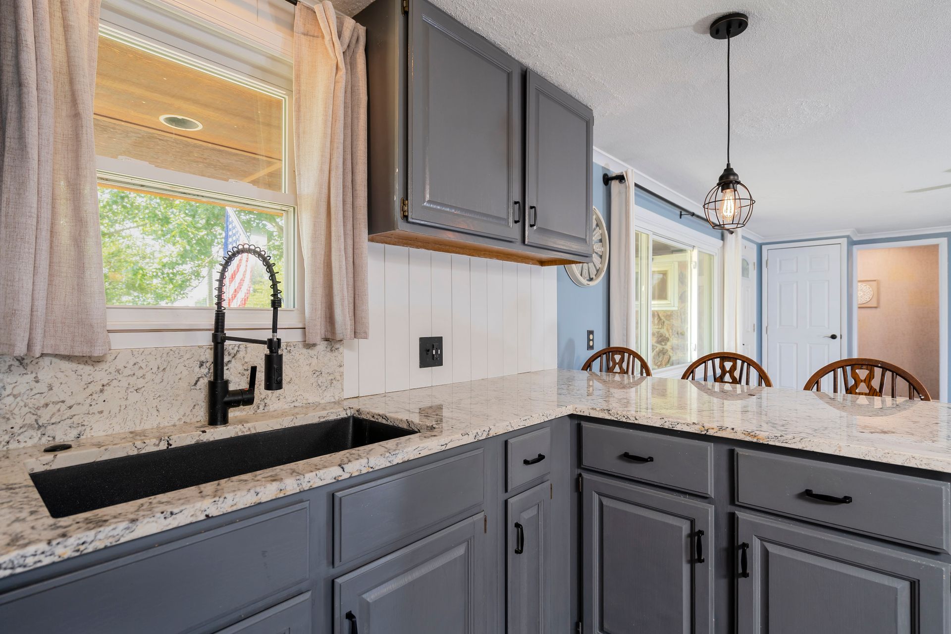 Modern kitchen with gray cabinets, white countertops, black sink, and breakfast bar stools