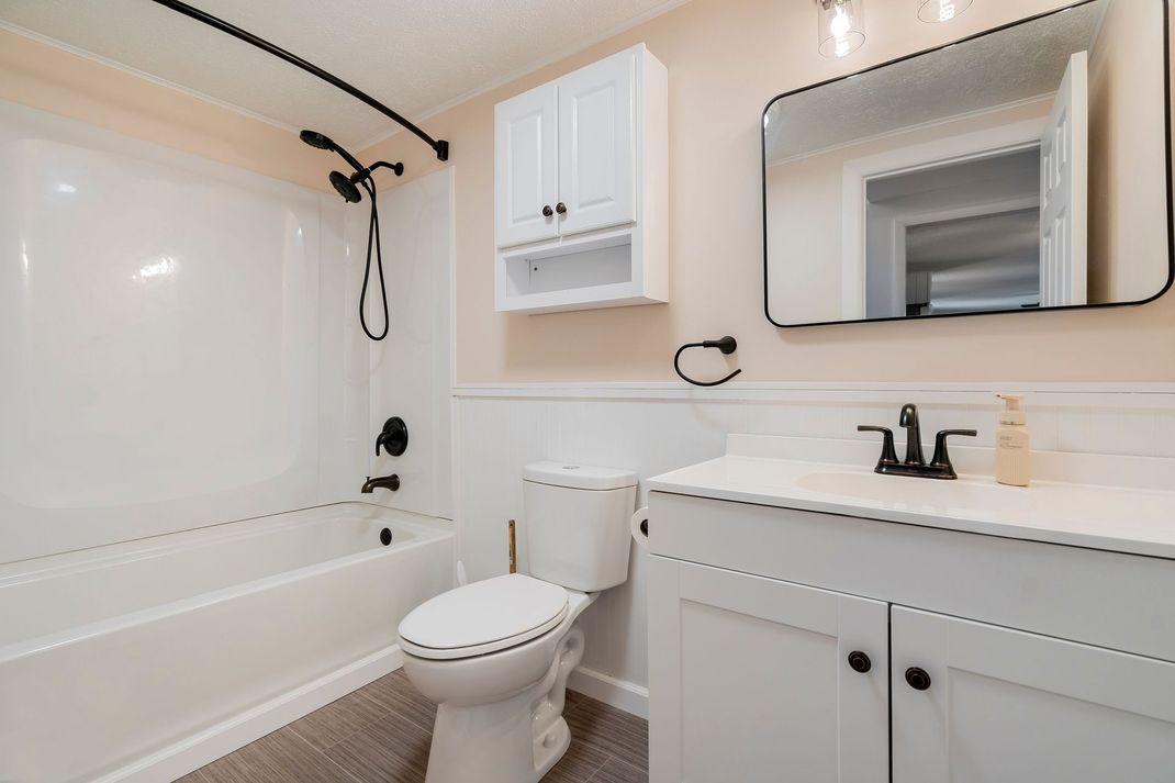 Bright white bathroom with tub, toilet, vanity, and mirror cabinet