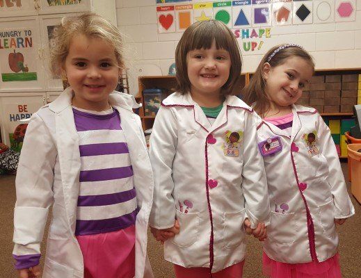 Three little girls dressed as doctors holding hands in a classroom