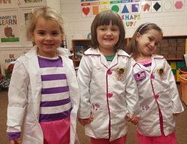 Three little girls dressed as doctors holding hands in a classroom