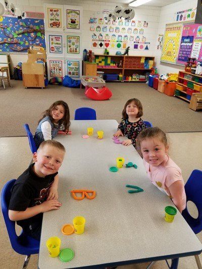 A group of children are sitting at a table in a classroom playing with play dough.