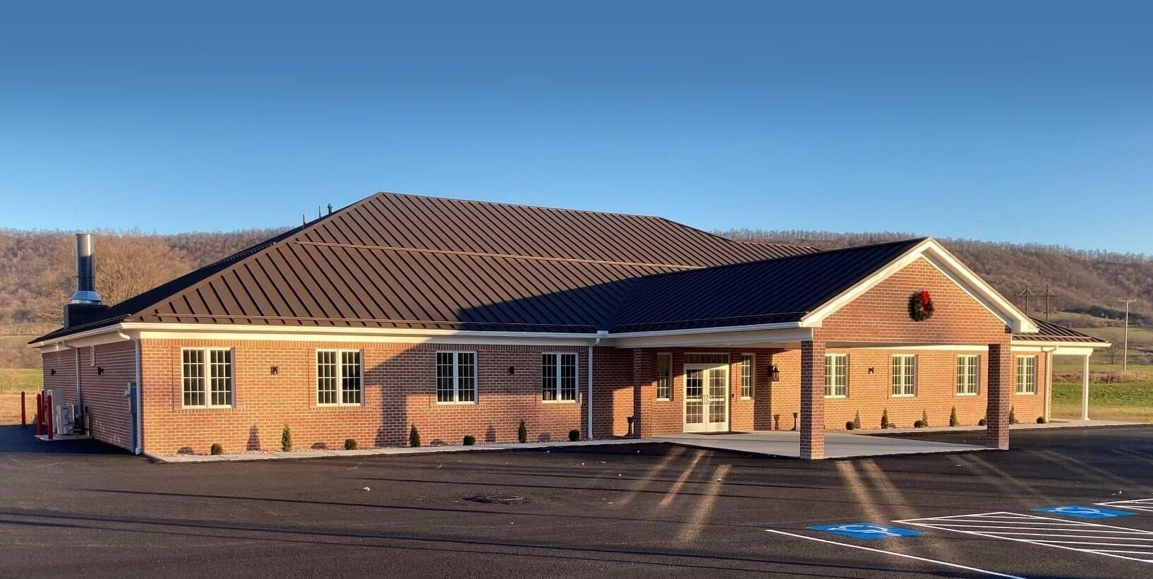 Brick community building with a red-tiled roof beside a paved parking lot under a clear blue sky