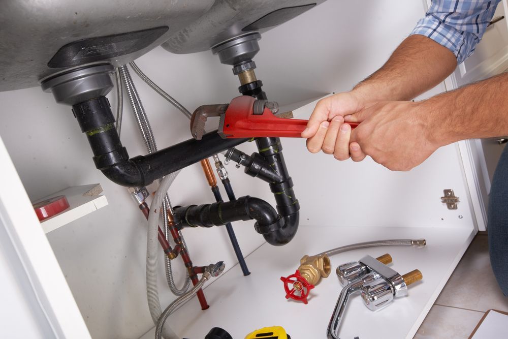 A Person Using A Red Pipe Wrench To Work On Black Drain Pipes — ATEC Plumbing Services in Morisset, NSW