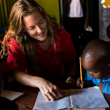 Dr. Angela Marick, life coach, sitting beside a child and guiding them as they write in a notebook.