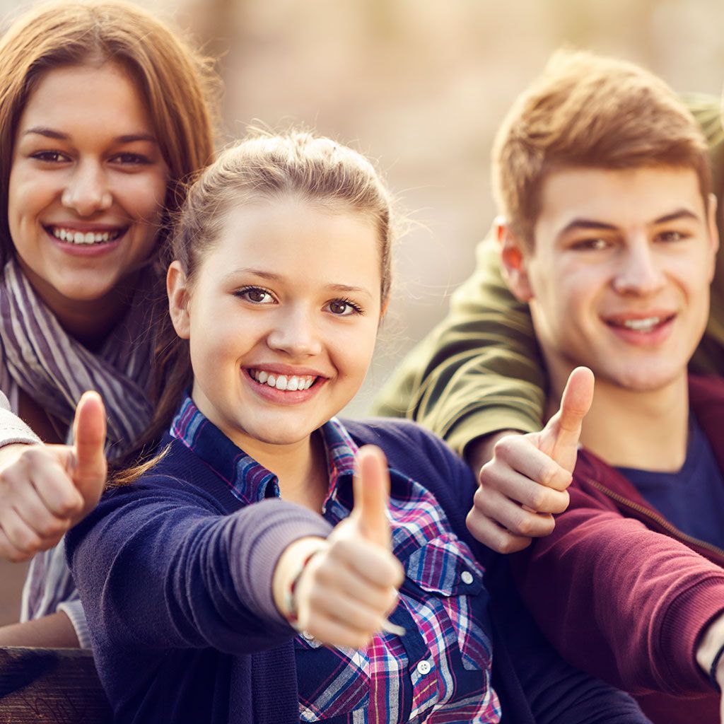 Tre giovani adulti sorridenti che alzano il pollice, all'aperto.