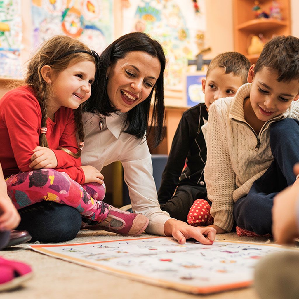 Insegnante e bambini sorridono mentre guardano un gioco sul pavimento.