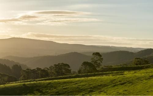 Sun is Shining Through the Clouds Over a Grassy Hillside With Mountains — GMT Builders Pty Ltd in Moss Vale, NSW