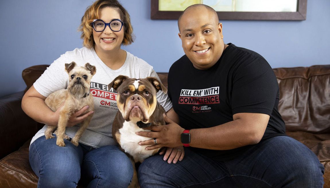 Two people on a couch holding two small dogs, smiling in a living room.