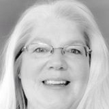 A black and white photo of a woman wearing glasses and smiling.