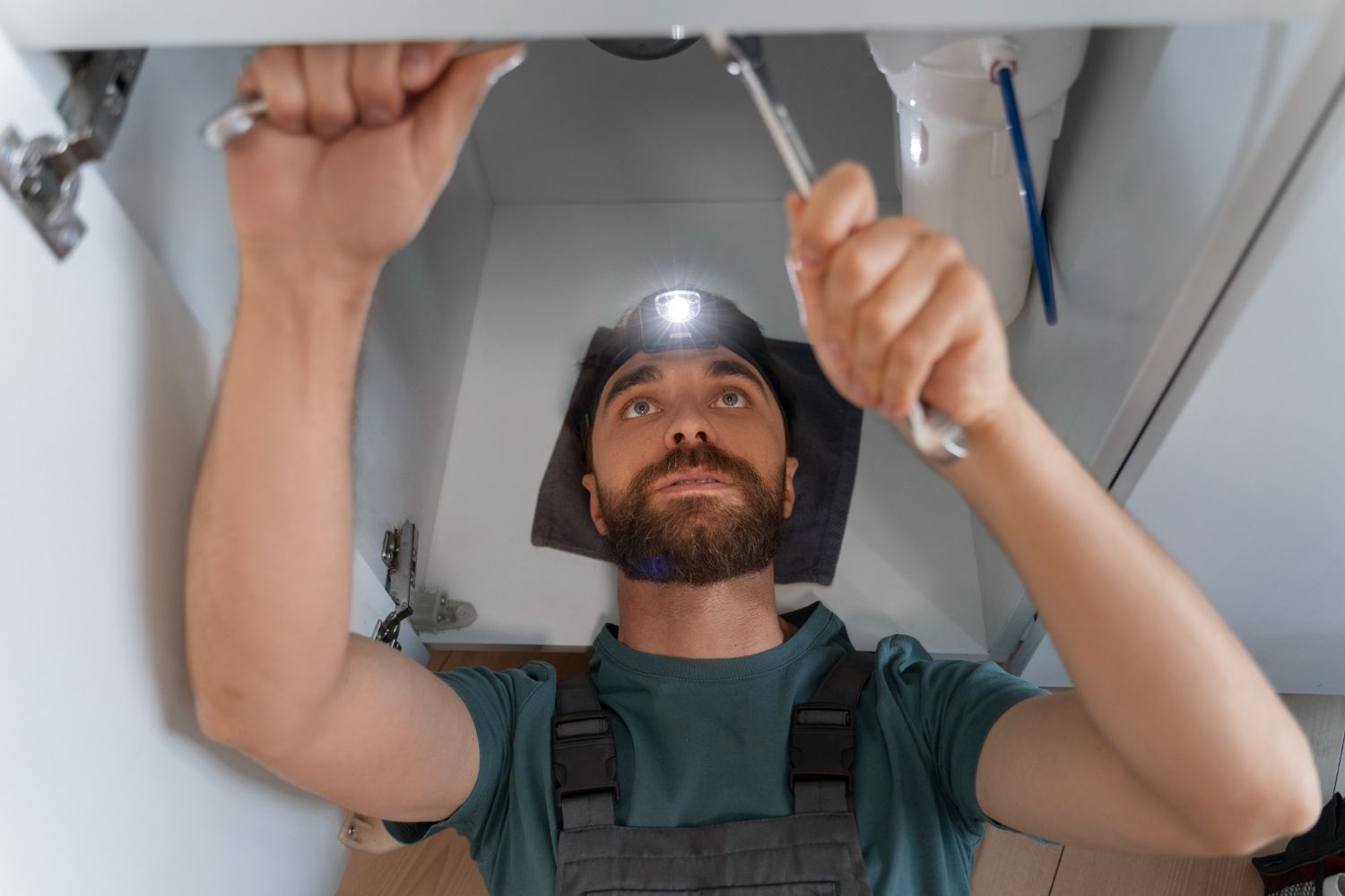 A worker with a headlamp works under a sink using a wrench to repair plumbing.