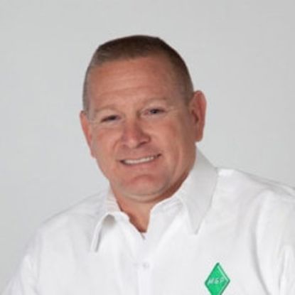 A person with a neutral expression wearing a white collared shirt with a small green logo on the chest against a gray background.