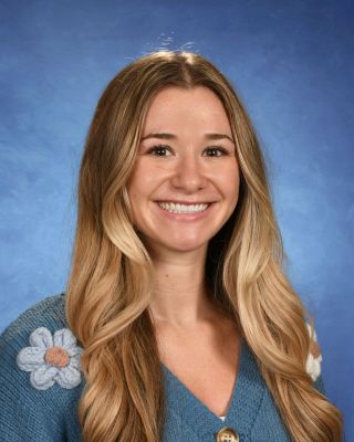 A young woman is smiling for a picture in front of a blue background.