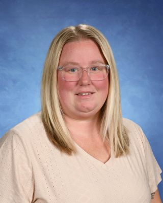 A woman in a blue shirt is smiling in front of a blue background.