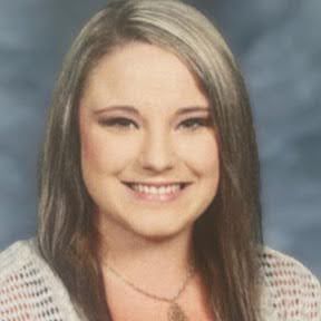 A woman is smiling for a picture and wearing a necklace.