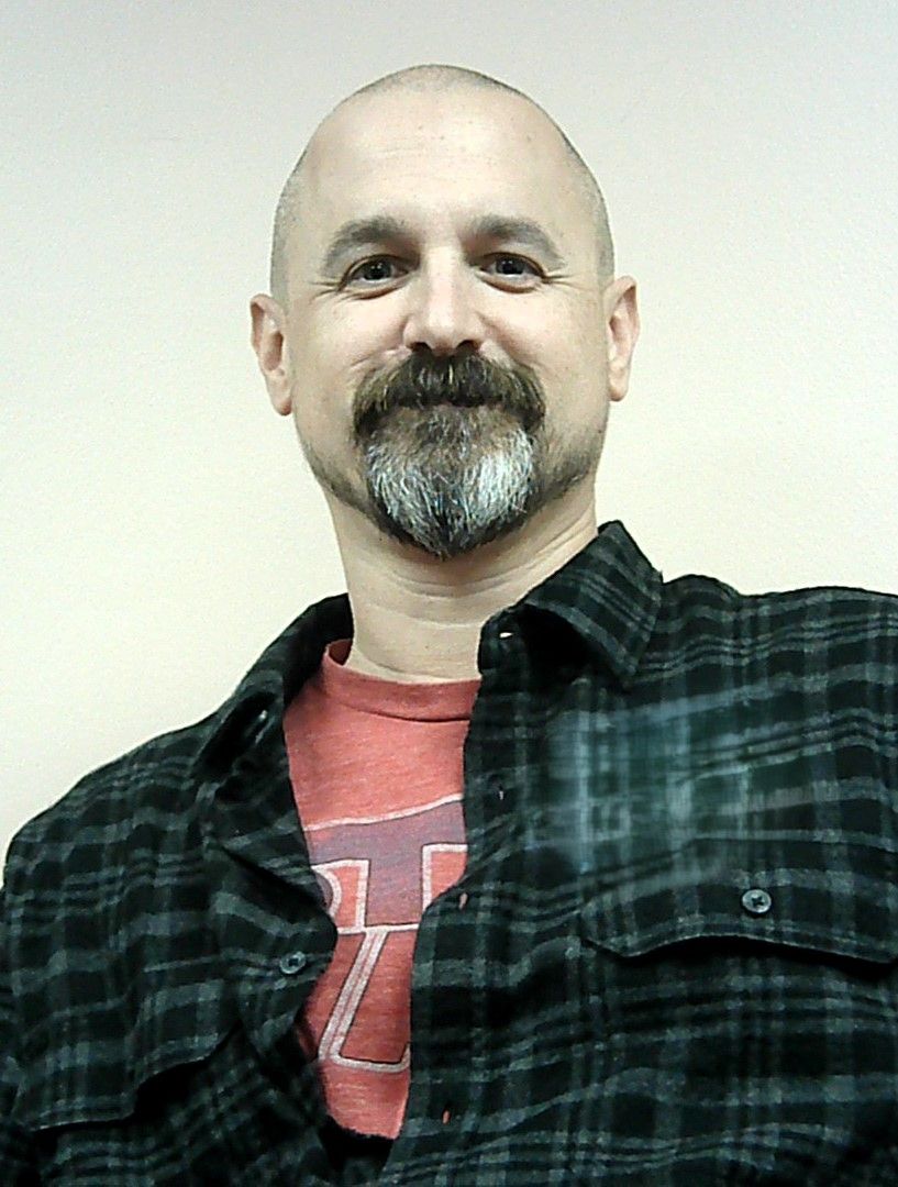 A bald man with a beard wearing a plaid shirt