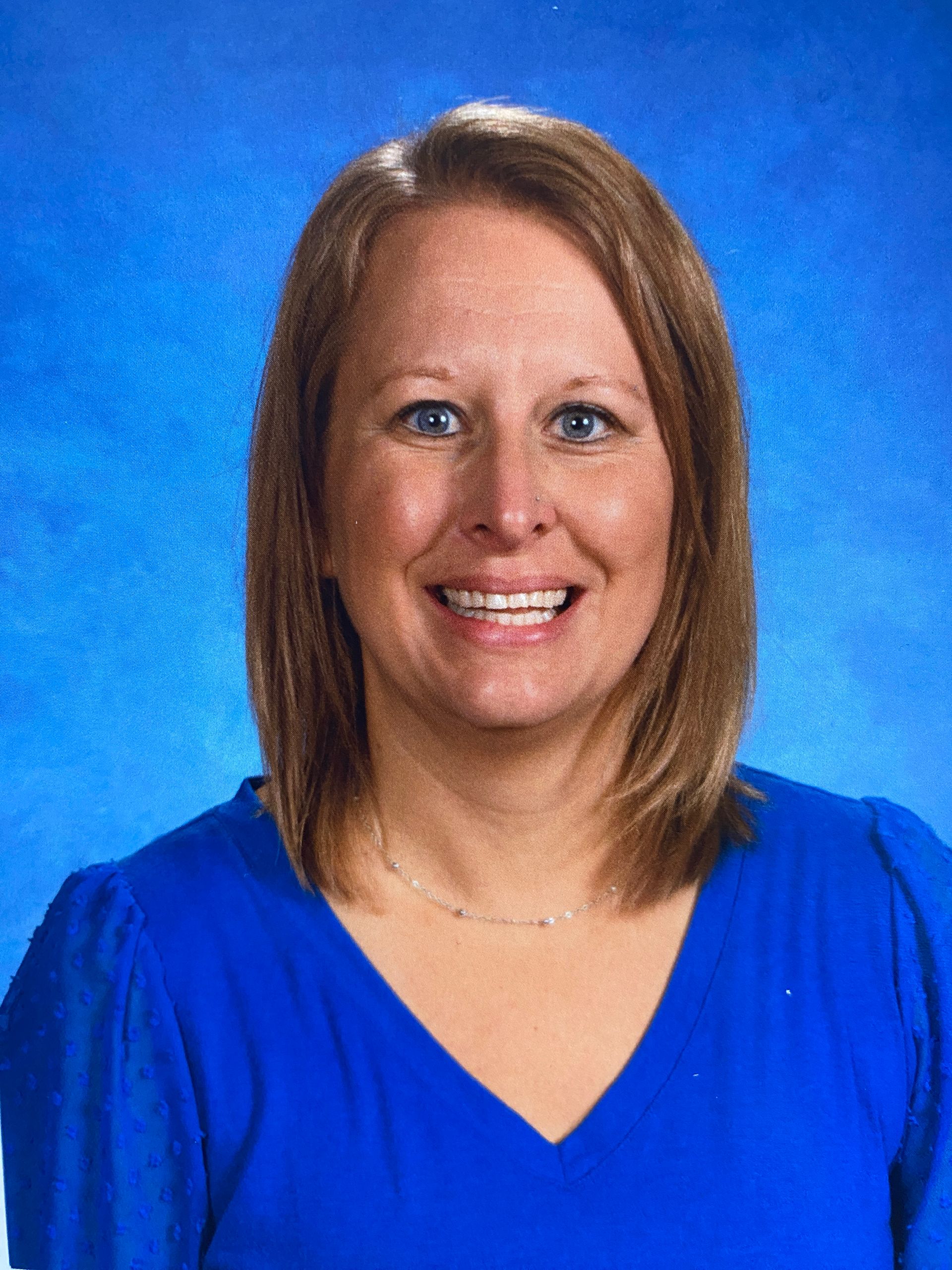 A woman in a blue shirt is smiling in front of a blue background.
