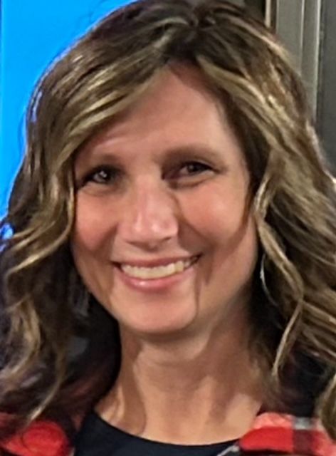 A woman in a plaid shirt is smiling for the camera.