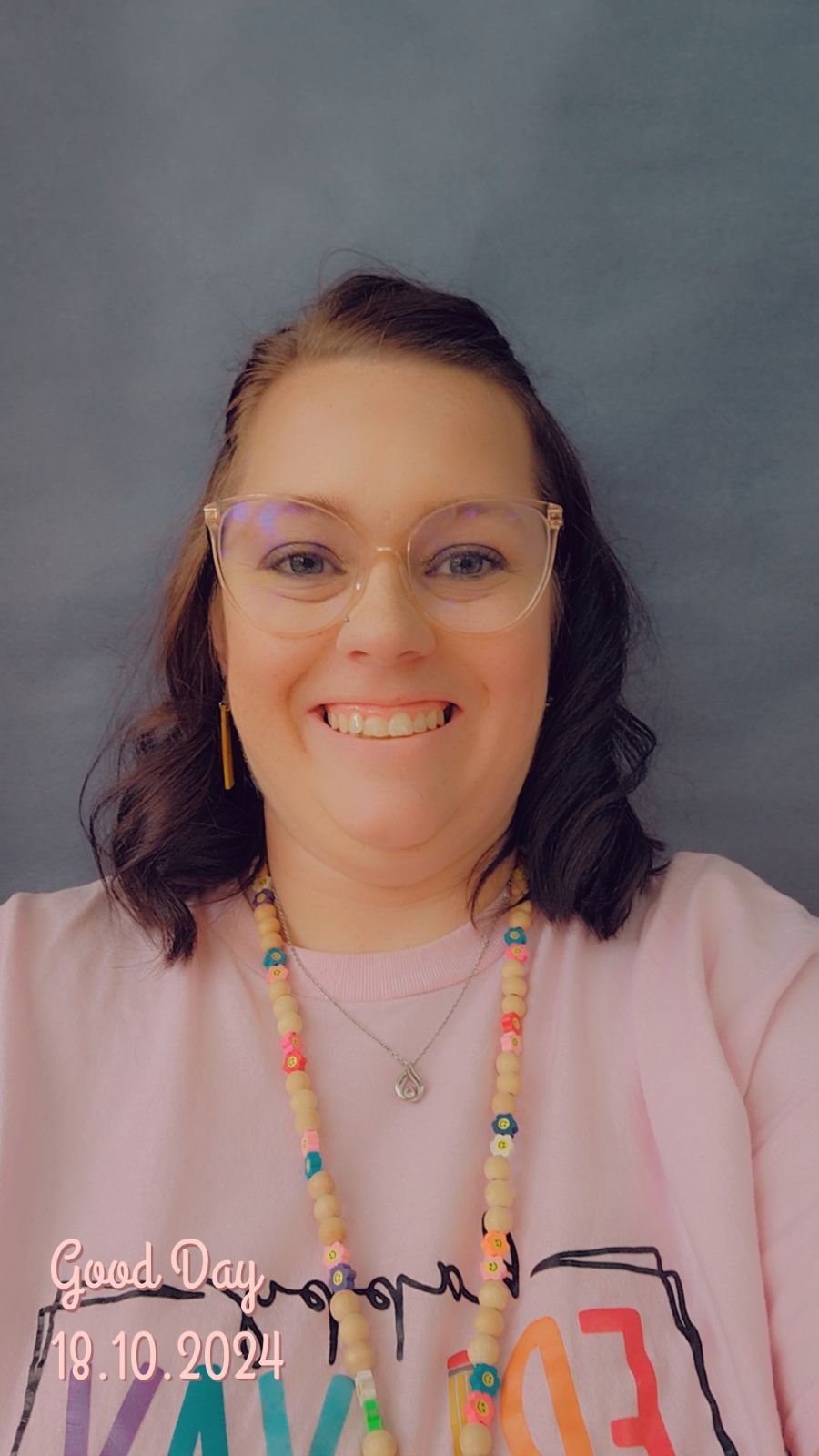 A woman wearing glasses and a pink shirt is smiling for the camera.