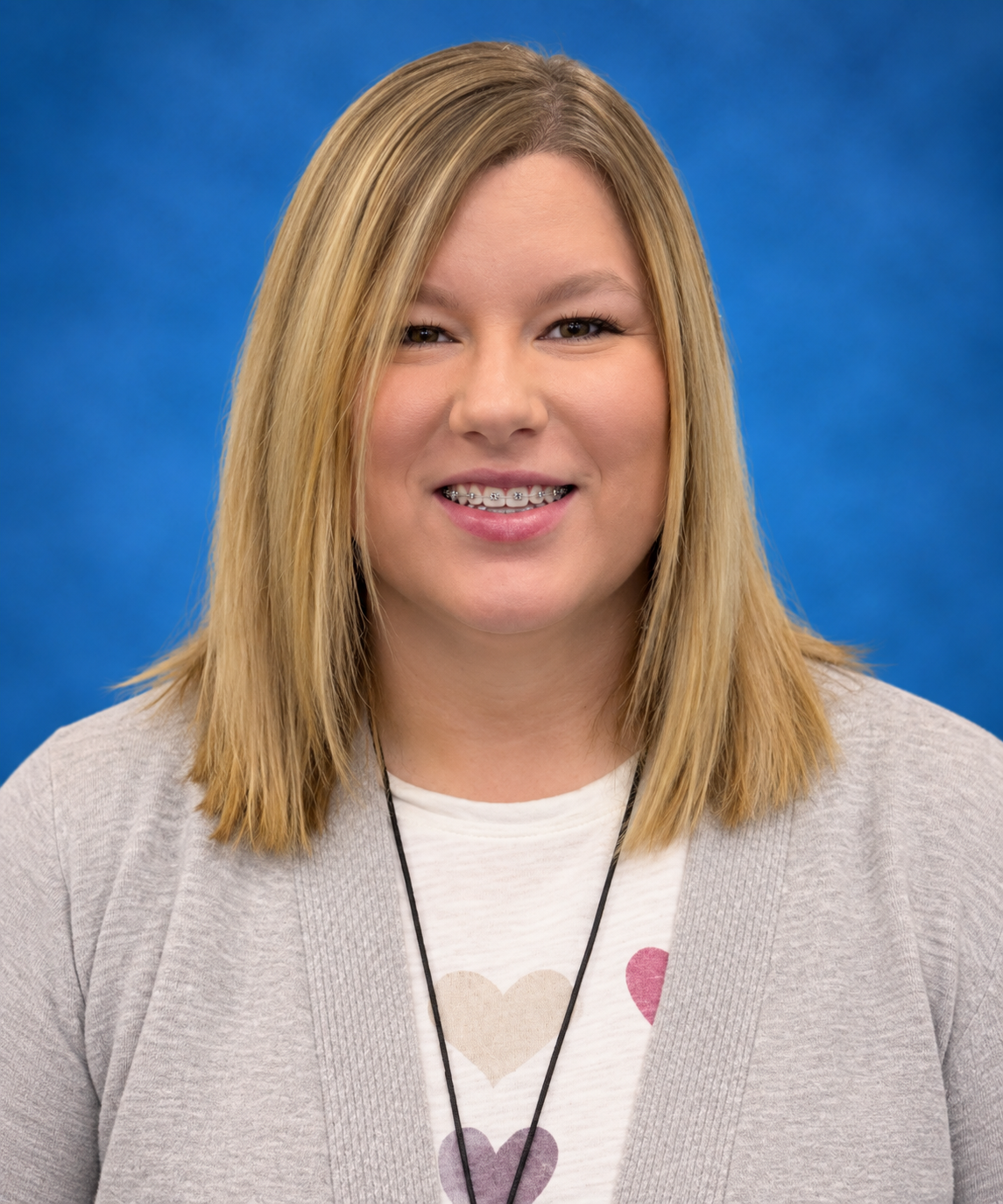 A woman wearing a sweater and a necklace with hearts on it is smiling.